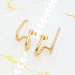 Ατσάλινα σκουλαρίκια Diplo σε χρυσό χρώμα, διακοσμημένα με λευκά στρας.